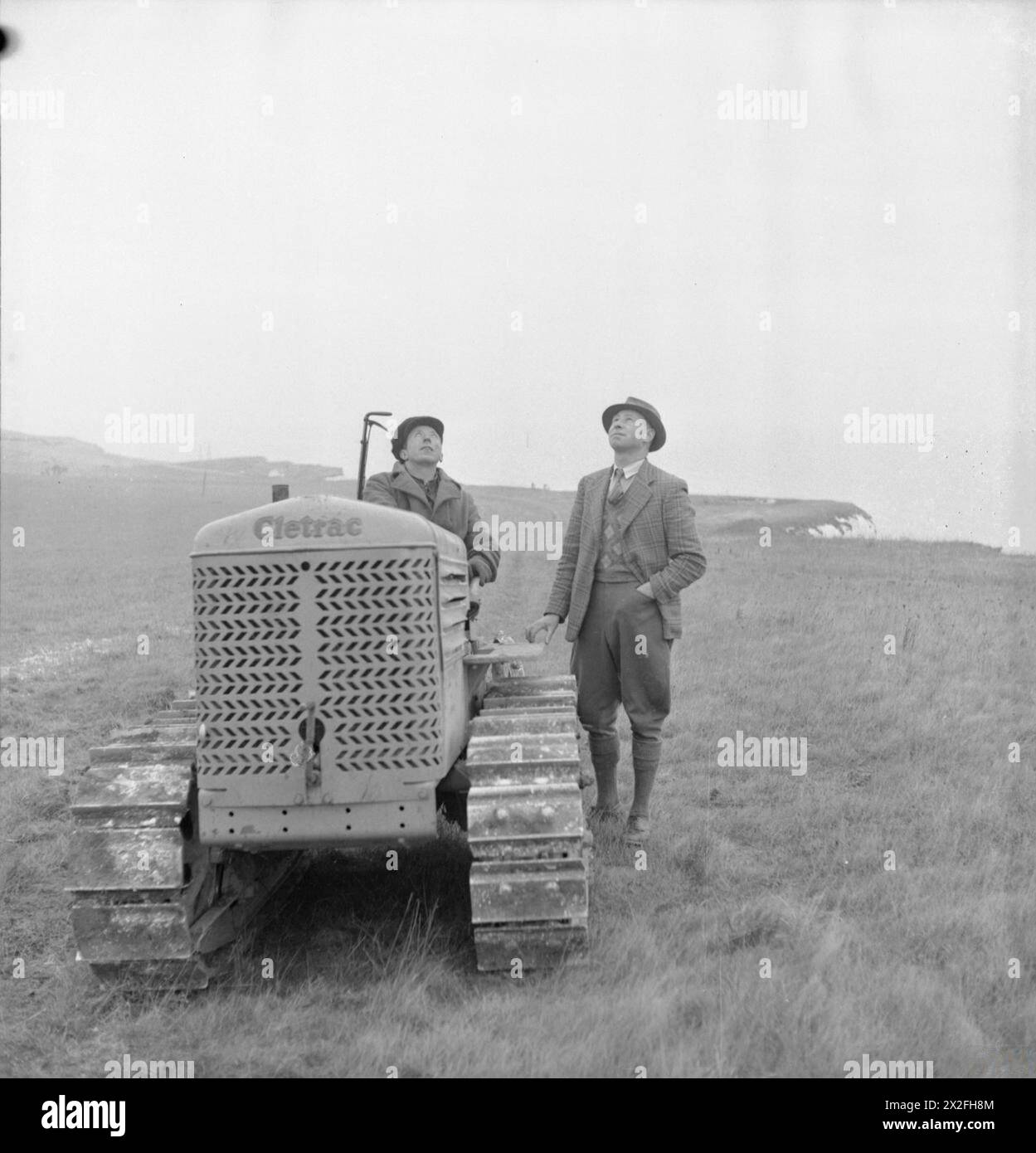 Le fermier Gilbert Mitchell et son chauffeur de tracteur C. Rogers travaillent dans les champs au bord des falaises blanches de Douvres vers 1944, observant un avion au-dessus de lui. Banque D'Images