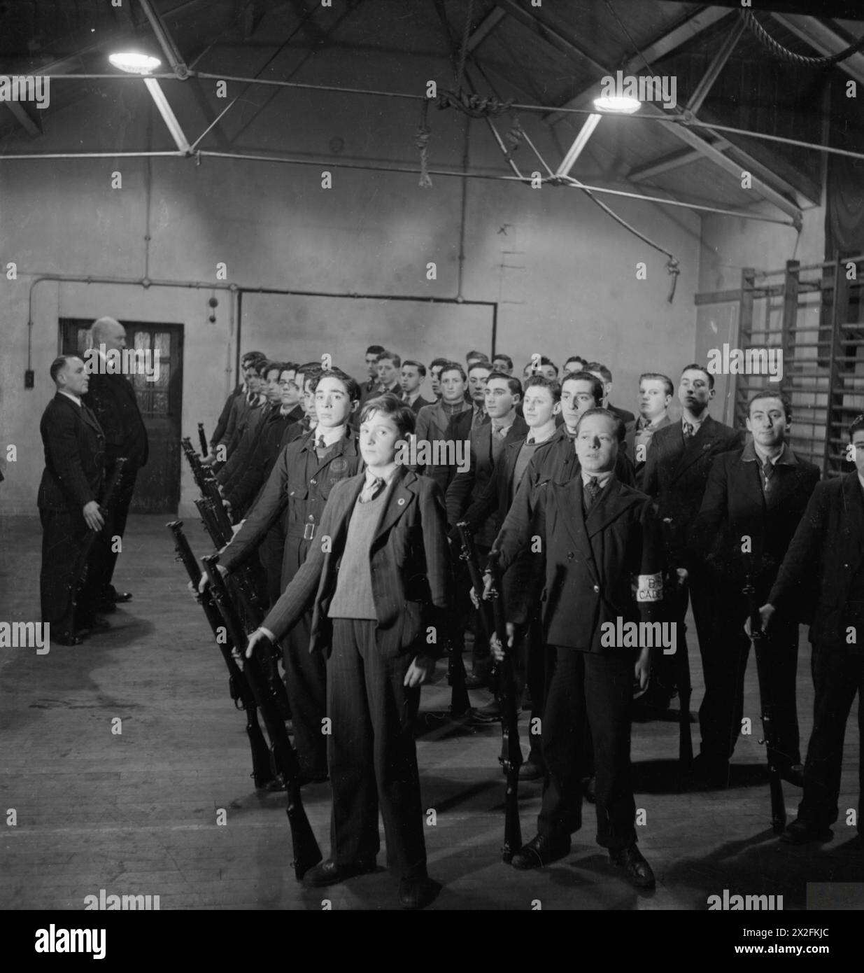 LONDON JEWISH IN WARTIME : THE WORK OF YOUTH CLUBS IN STEPNEY, LONDON, 1942 - Boy Cadets de la Bernhard Baron Company, 1st Battalion Royal Fusiliers, City of London Cadets se tiennent à l'attention, surveillés par leur commandant le capitaine Basil Q Henriques JP, pendant l'exercice au fusil dans le gymnase de la colonie juive Bernhard Baron sur Berner Street Banque D'Images