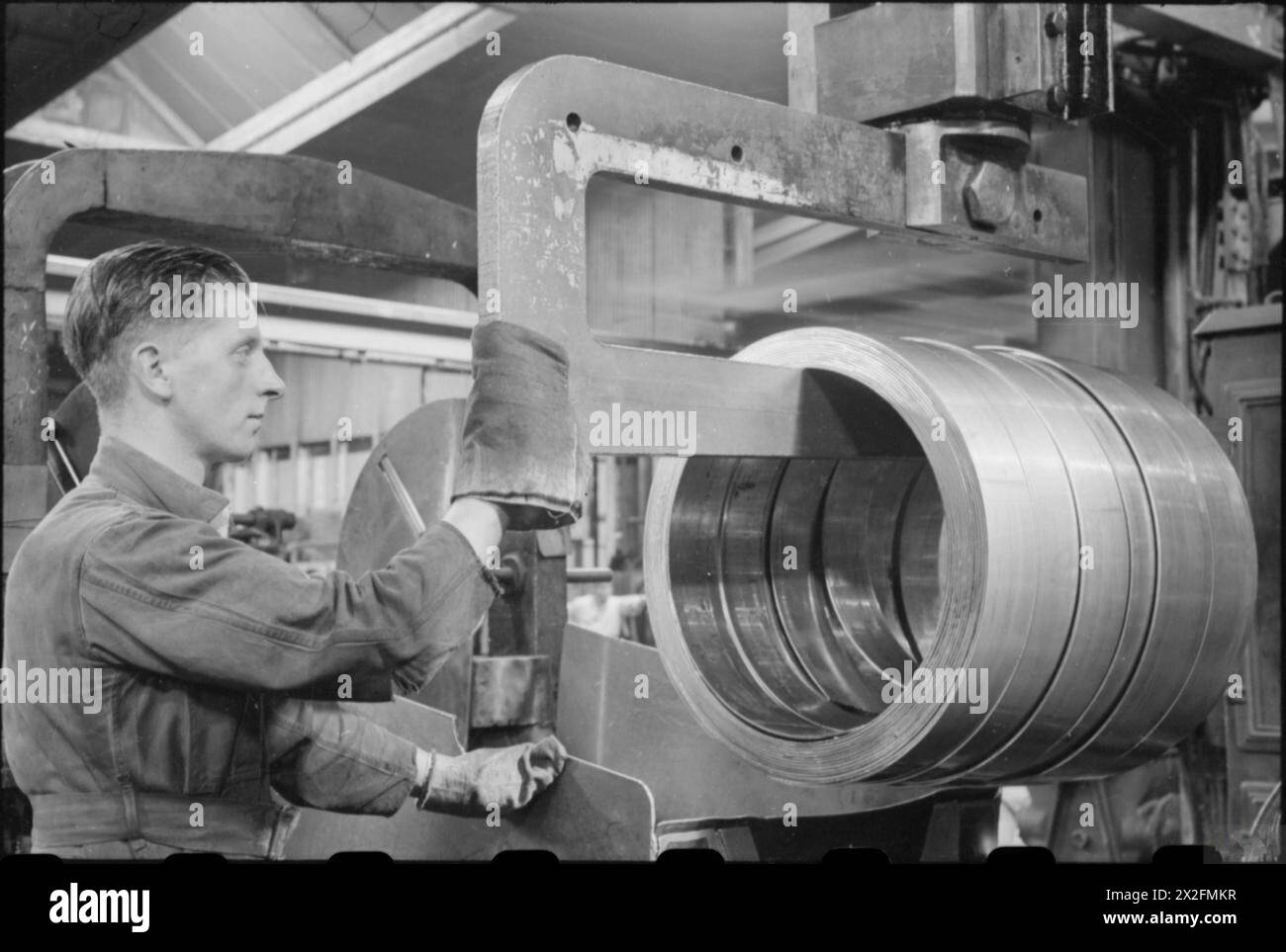 INDUSTRIE DE GUERRE, Royaume-Uni, c 1942 - Un ouvrier de guerre enlève des bobines de laiton d'une machine de cisaillement dans une usine, quelque part en Grande-Bretagne Banque D'Images