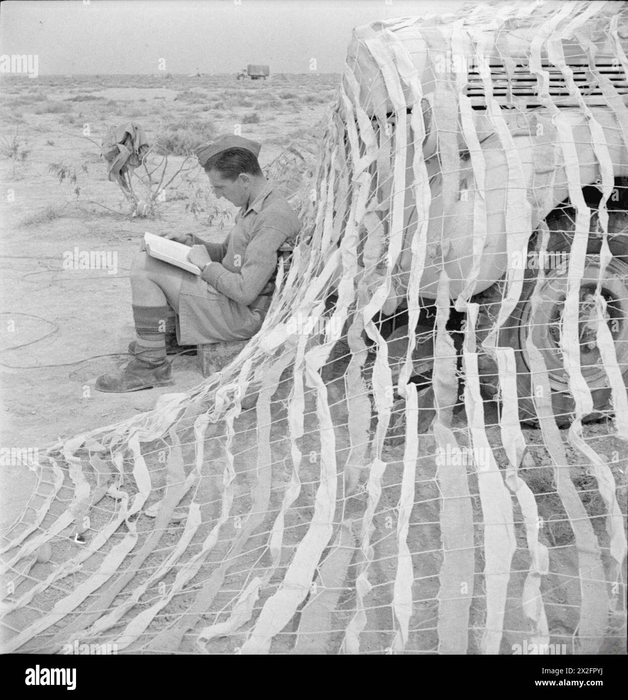 CECIL BEATON DANS LE MOYEN-ORIENT FÉVRIER-JUILLET 1942 - Une soudure est assis lisant un livre à l'extérieur d'une tente camouflée, désert occidental Banque D'Images