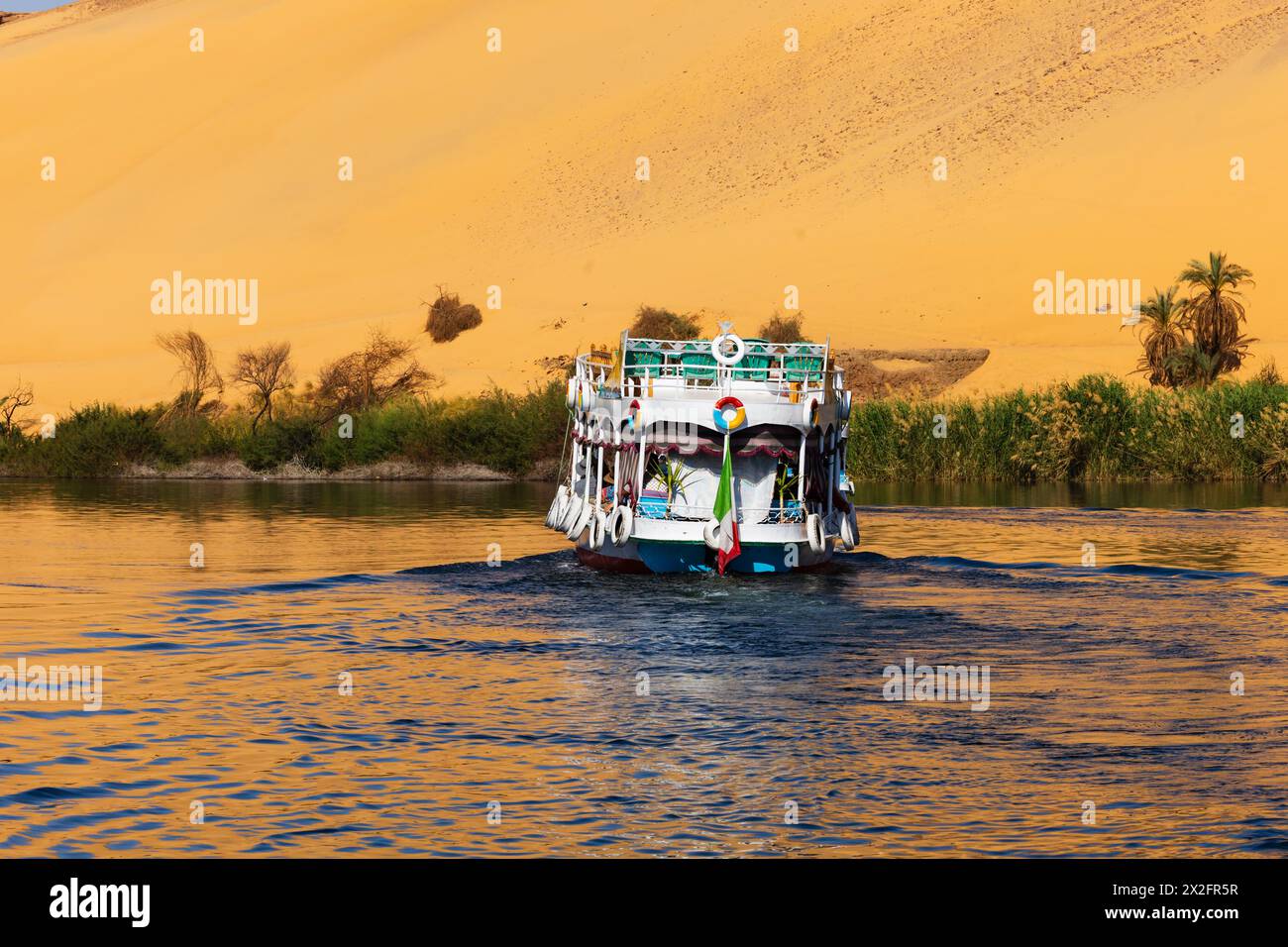 Bateau fluvial touristique sur le Nil, avec des reflets dorés du désert du Sahara, Assouan, Egypte Banque D'Images