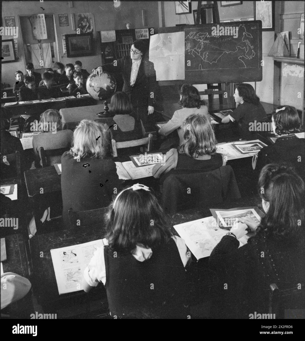 Des élèves de treize ans de la Peckham Central School à Londres apprennent l'URSS auprès de leur professeur lors d'une leçon de géographie en 1943, avec un globe et une carte sur le tableau noir, et les élèves assis séparément par sexe. Banque D'Images