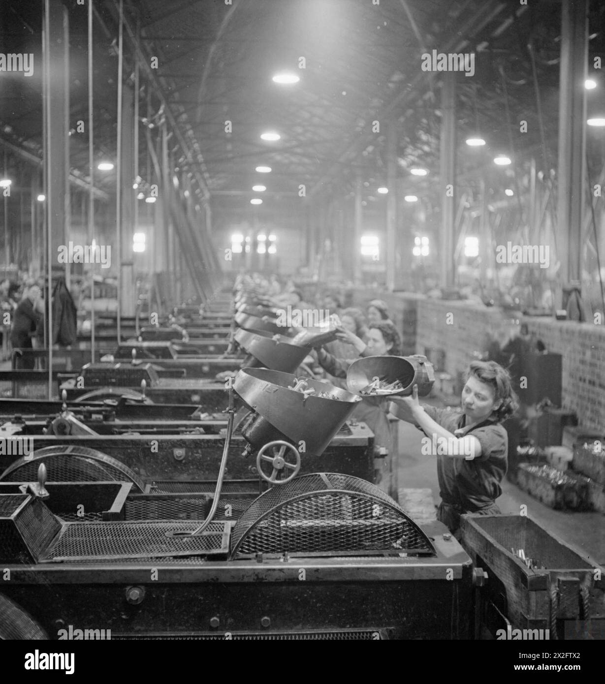 En Grande-Bretagne en 1941, des femmes sont représentées engagées dans la production d'obus dans une usine, accomplissant des tâches telles que la tête d'étuis d'obus dans le cadre de l'industrie des munitions en temps de guerre. Banque D'Images