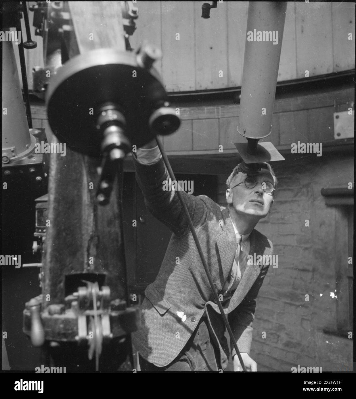 THE ROYAL OBSERVATORY : LA VIE QUOTIDIENNE AU ROYAL OBSERVATORY, GREENWICH, LONDRES, ANGLETERRE, ROYAUME-UNI, 1945 - Un scientifique de l'Observatoire royal de Greenwich attend une pause dans les nuages pour prendre une photo du soleil à l'aide d'un haliographe. Selon la légende originale, cela se produit quotidiennement, si le temps le permet, depuis 1873 et « les photographies sont mesurées pour obtenir les zones et les positions des taches et autres marques sur le Soleil, fournissant ainsi un enregistrement continu de l'activité du Soleil » Banque D'Images