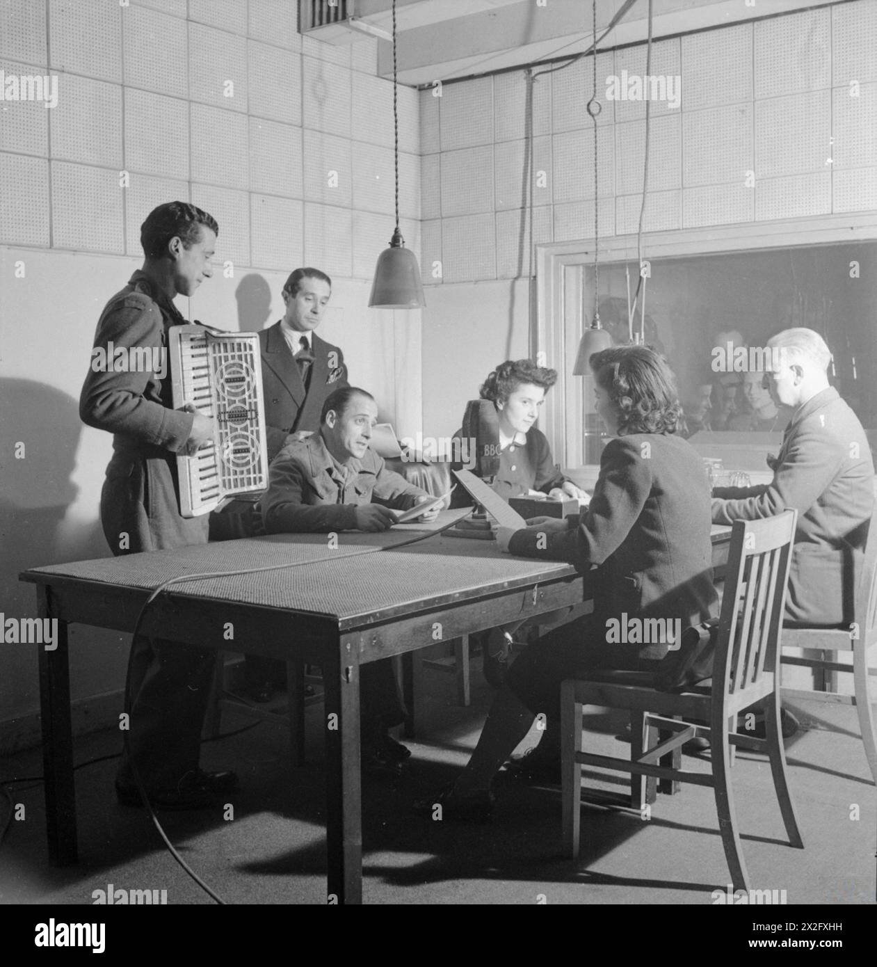 PRISONNIERS DE GUERRE ITALIENS EN GRANDE-BRETAGNE : LA VIE QUOTIDIENNE DANS UN CAMP de prisonniers de GUERRE ITALIENS, ANGLETERRE, Royaume-Uni, 1945 - depuis un studio de la BBC, le maestro Aldo Morbio et Guido Leoni, prisonniers de guerre italiens, participent à l'émission hebdomadaire 'The Camp Journal' qui reflète la vie au camp de travailleurs N.144 près de Londres. L'un des hommes joue de l'accordéon. Deux femmes et plusieurs autres hommes peuvent également être vus assis autour de la table, au centre de laquelle se trouve le grand microphone BBC Banque D'Images