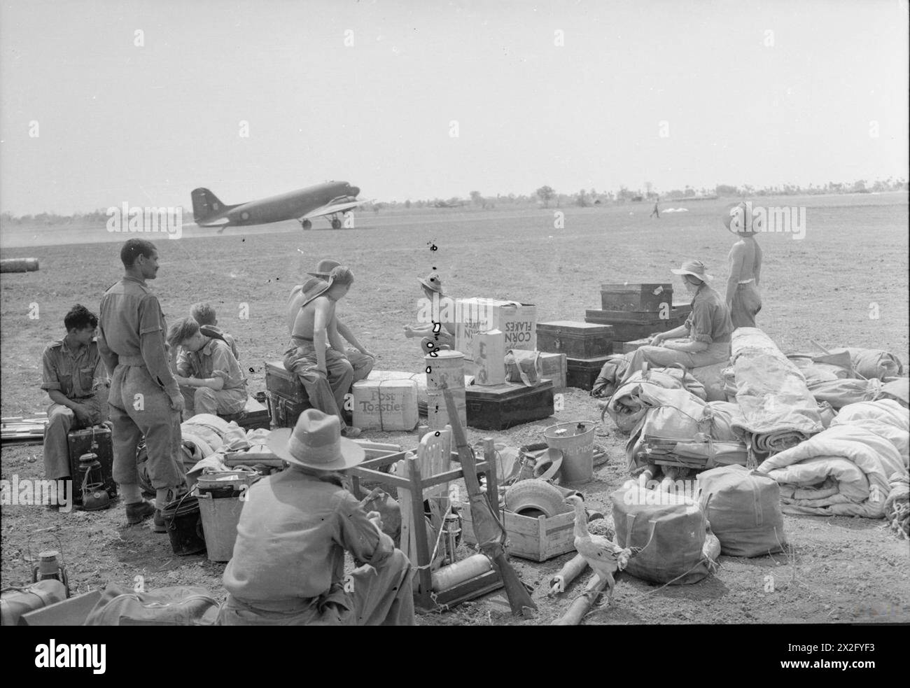 OPÉRATIONS DE LA ROYAL AIR FORCE EN EXTRÊME-ORIENT, 1941-1945 - entouré d'un assortiment de bagages, de tentes, de boîtes et de poulets, le personnel d'un escadron Spitfire de la RAF qui se déplace vers un autre aérodrome dans le centre de la Birmanie, regardez un Douglas Dakota Mark III du No. 117 Squadron RAF décoller chargé d'équipement pour leur nouvelle base de l'armée britannique, Royal Flying corps, Training Sqdn, 35 Banque D'Images