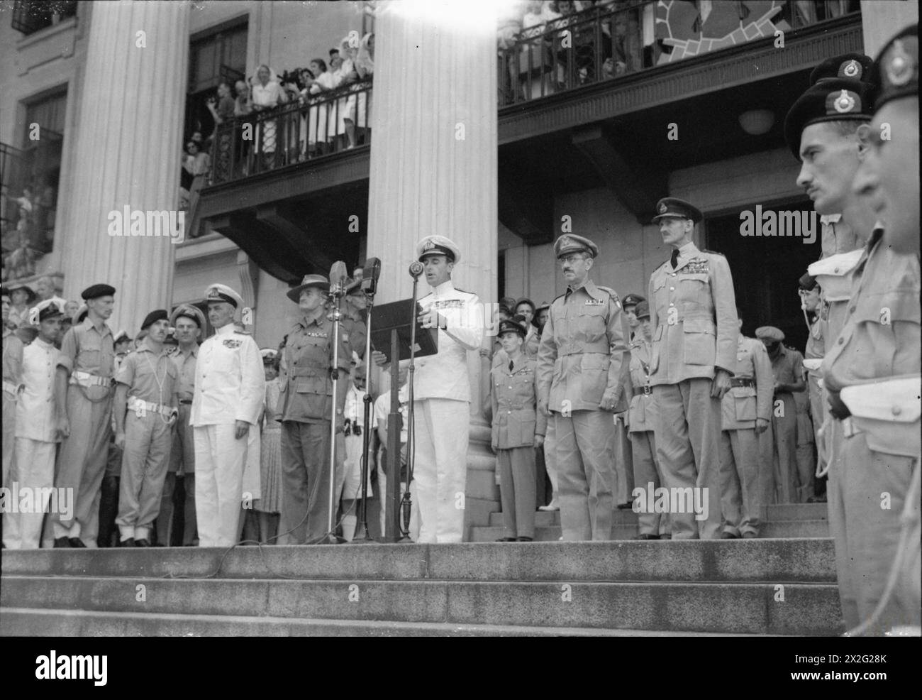 SIGNATURE DE LA REDDITION JAPONAISE À SINGAPOUR, 1945 - L'amiral Lord Louis Mountbatten prononce un discours public depuis les marches des bâtiments municipaux de Singapour lors de la cérémonie de reddition. À gauche de Mountbatten se trouvent l'amiral Power et le lieutenant-général Slim et à droite le lieutenant-général Wheeler et le maréchal en chef de l'air Sir Keith Park Mountbatten, Louis Francis Albert Victor Nicholas George, Power, Arthur John, Slim, William Joseph, Wheeler, Raymond Albert, Park, Keith Rodney Banque D'Images