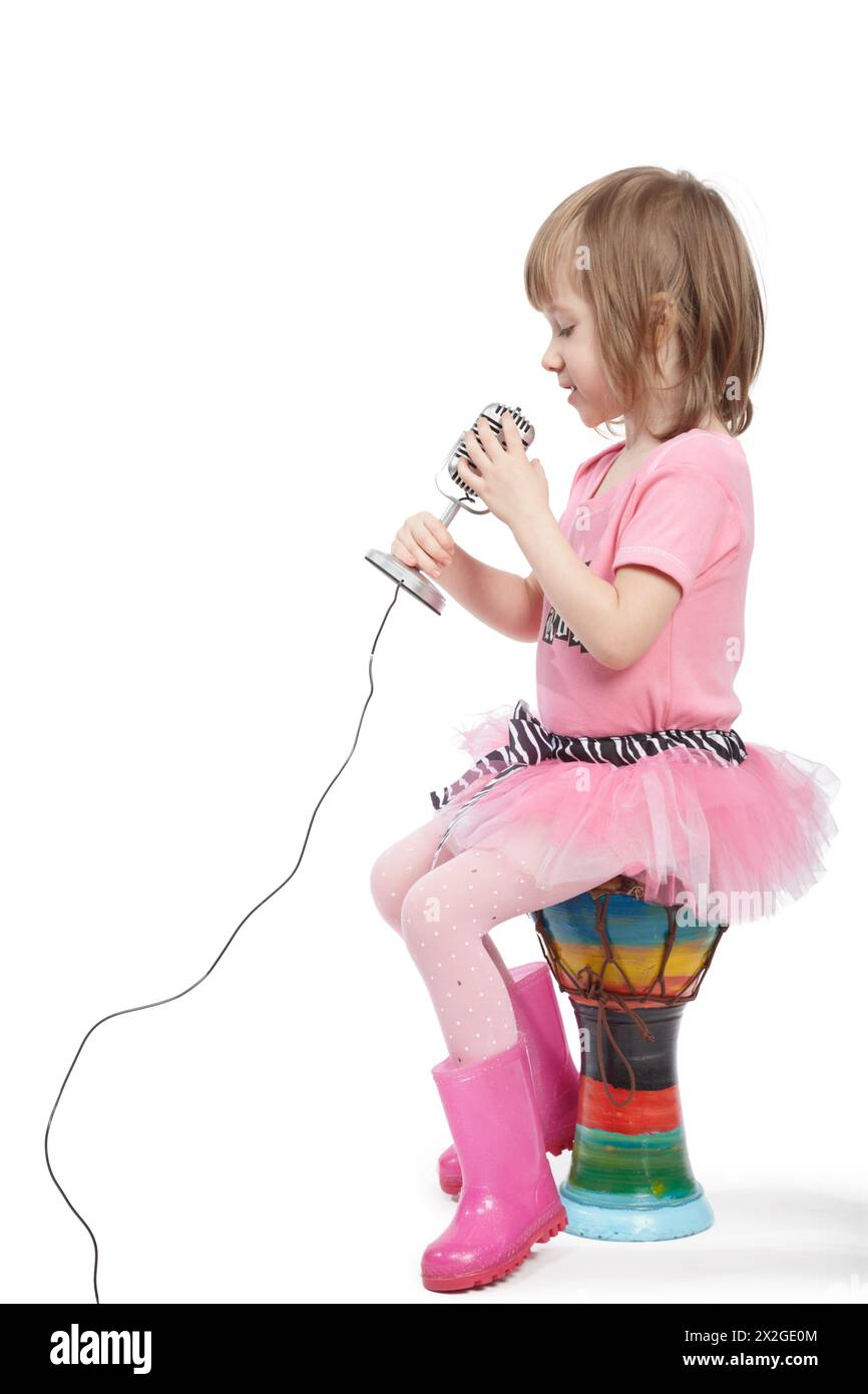 Petite fille en fille dans une robe rose et dans un gumboots rose s'assoit sur le djembé et chante dans le microphone. Banque D'Images