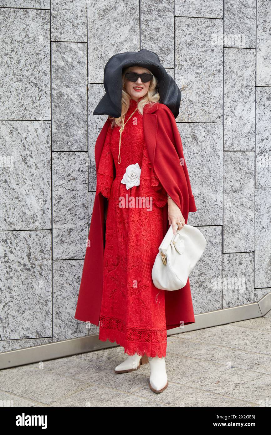 MILAN, ITALIE - 24 FÉVRIER 2024 : femme avec robe rouge et manteau avant le défilé Ermanno Scervino, dans le style de la semaine de la mode de Milan Banque D'Images