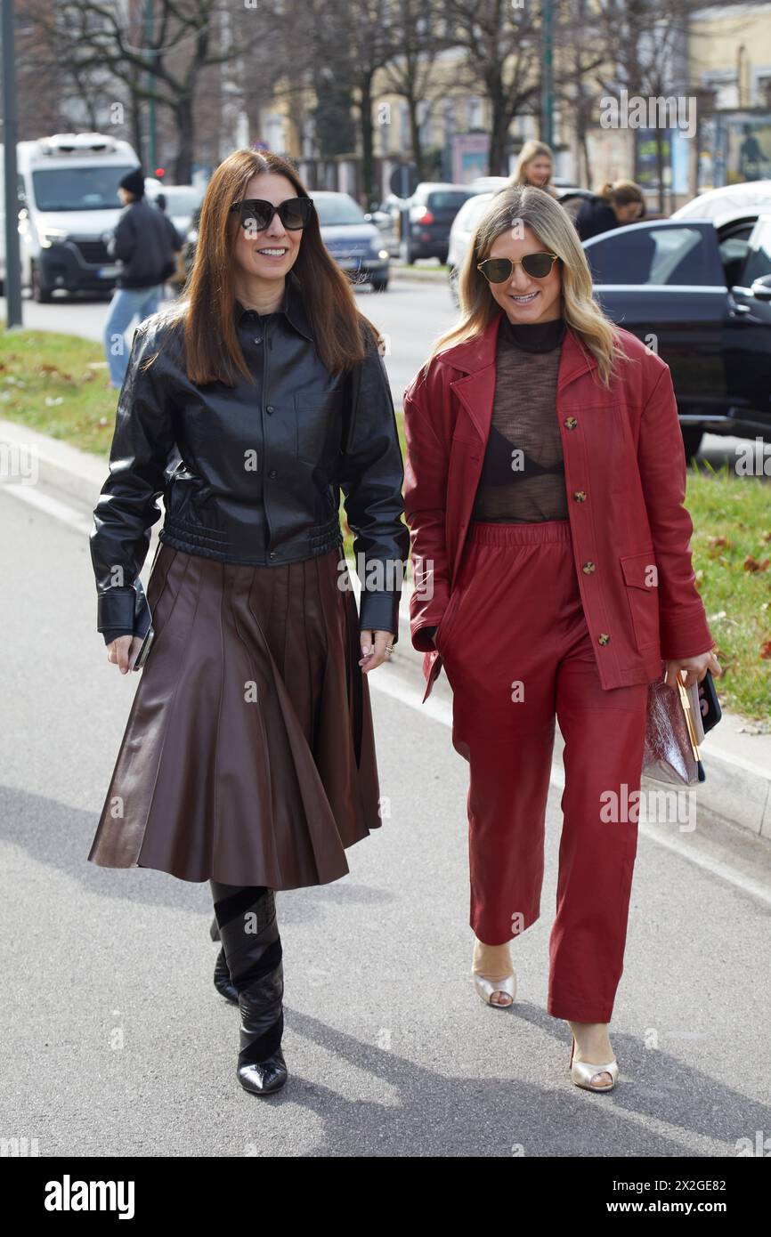 MILAN, ITALIE - 24 FÉVRIER 2024 : femmes avec veste en cuir noir, jupe marron et costume rouge avant le défilé Ferragamo, rue Milan Fashion week Banque D'Images