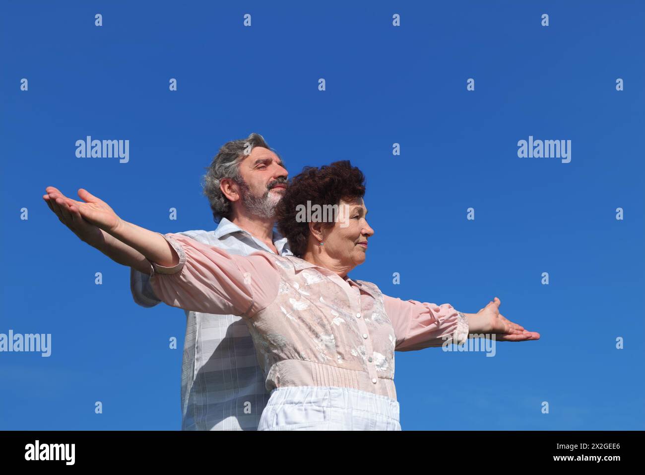 vieil homme et femme debout, souriant et regardant de côté, les mains écartées, ciel bleu Banque D'Images