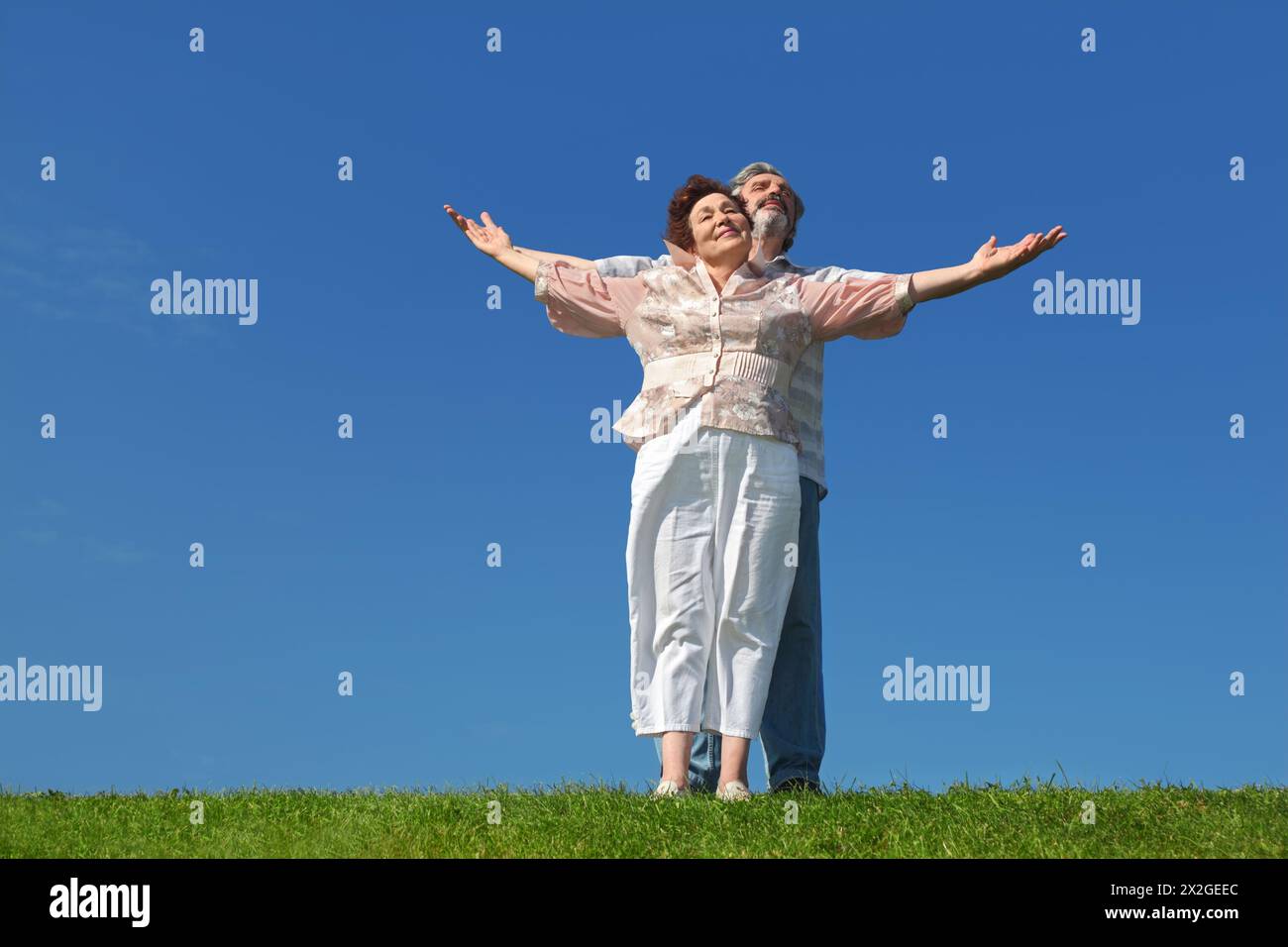 vieil homme et femme debout et souriant et, mains écartées, corps entier, ciel bleu Banque D'Images