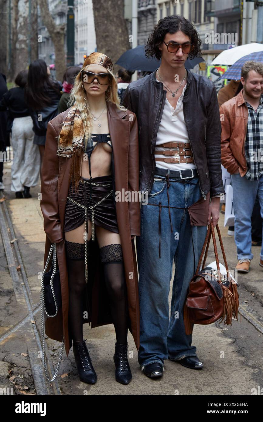 MILAN, ITALIE - 24 FÉVRIER 2024 : femme et homme avec trench-coat marron, bas noirs et pantalon en denim bleu avant le défilé Dolce et Gabbana Banque D'Images