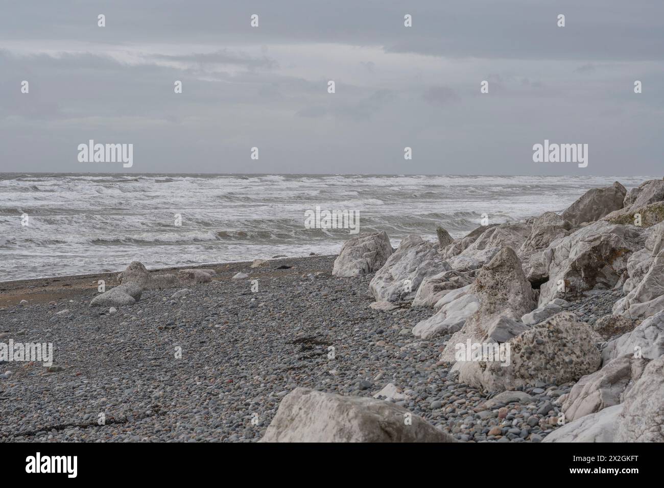 Rochers blancs sur une plage pierreuse sous le ciel gris avec des vagues roulantes d'eau vive, paysage marin silencieux atmosphérique Banque D'Images