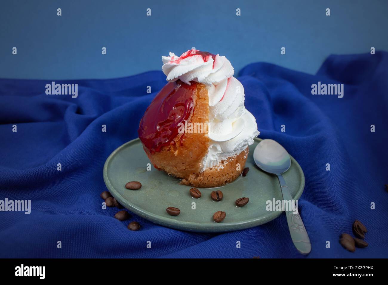 Gâteau Savarin avec glaçage rouge et crème fouettée sur tissu bleu Banque D'Images