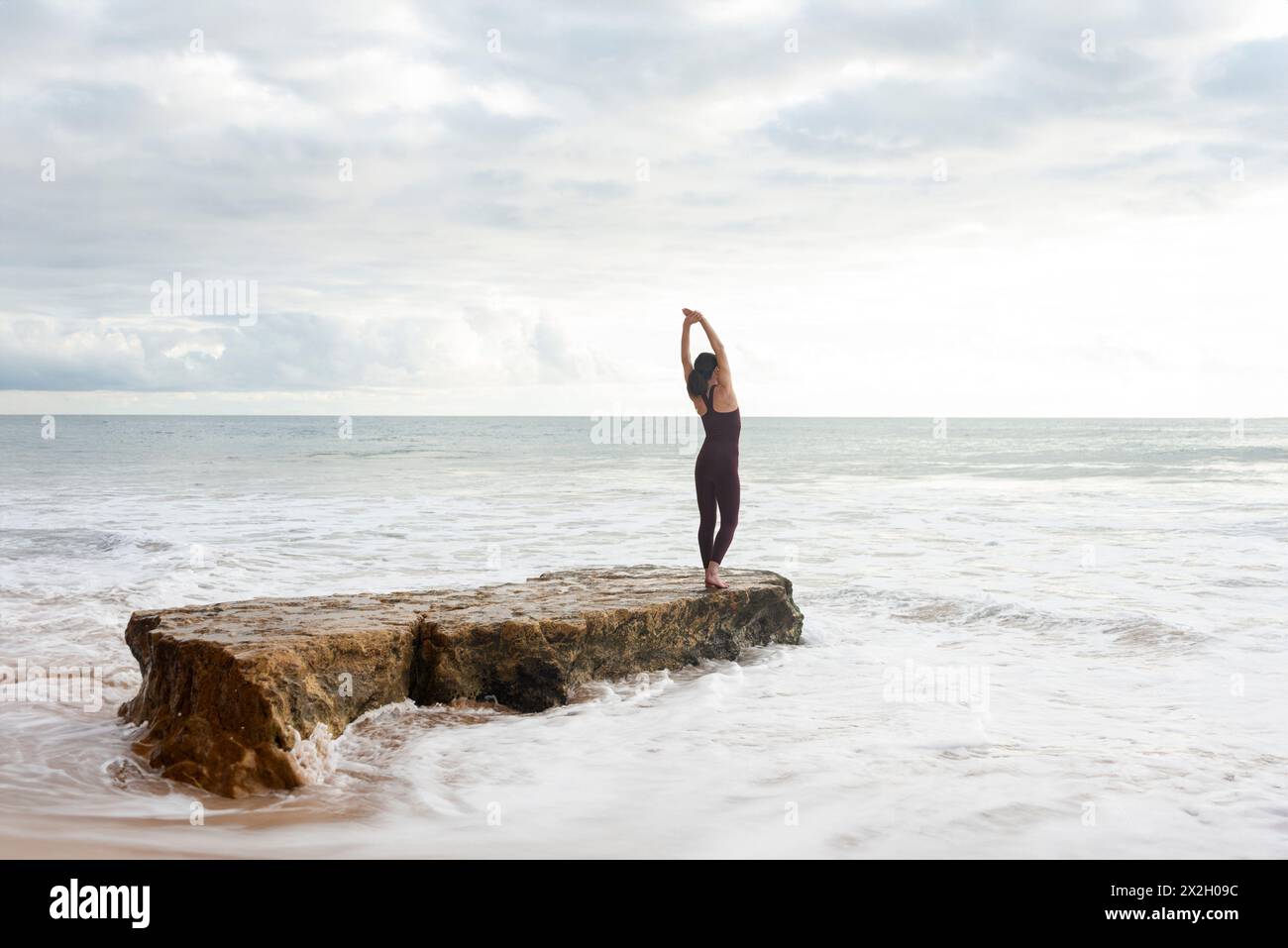 femme nageuse libre faisant un exercice d'étirement sur un rocher avant d'entrer dans la mer. Banque D'Images