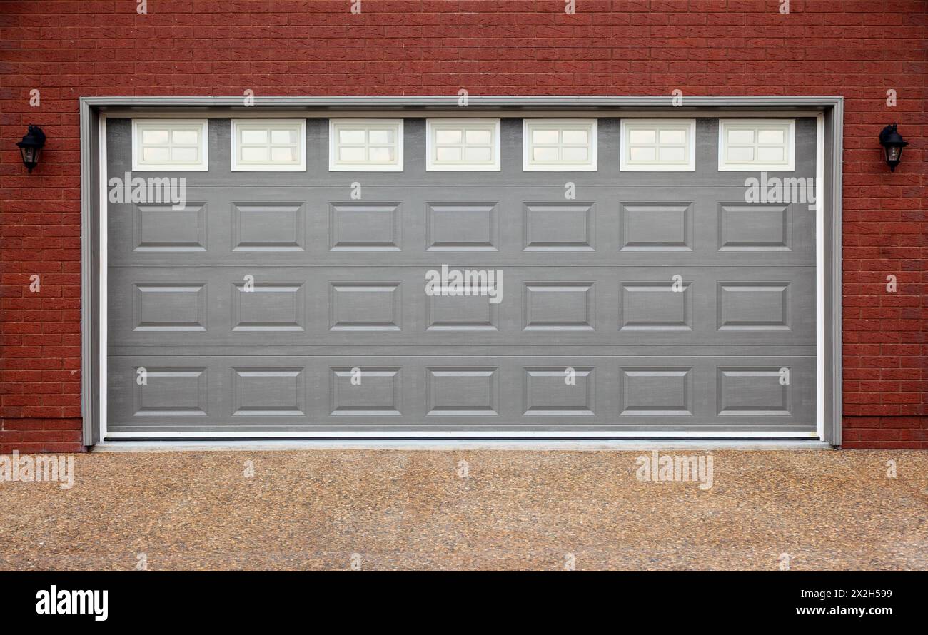 Grand garage avec portes grises, mur de briques et allée en asphalte Banque D'Images