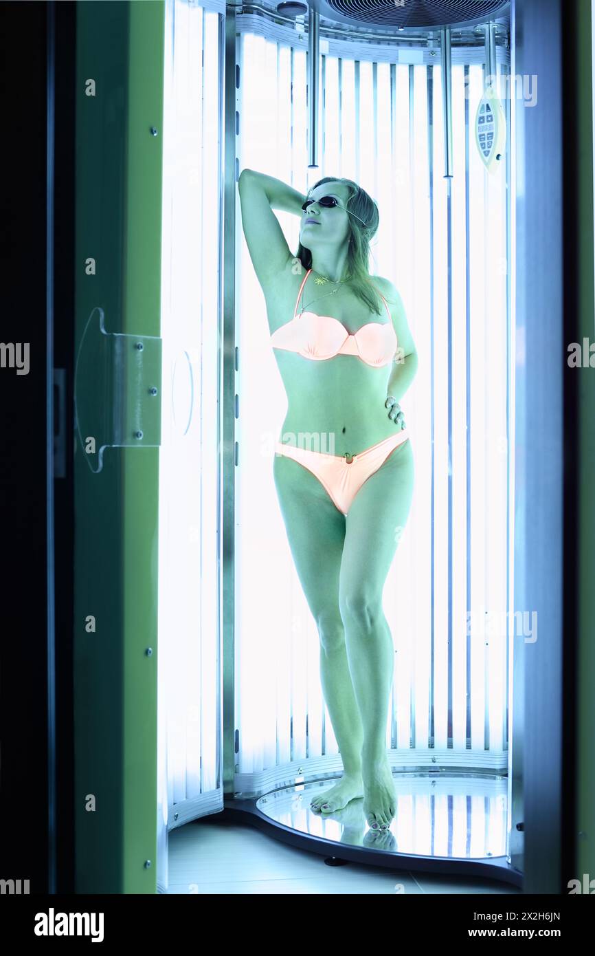 Femme vêtue d'un maillot de bain orange et de lunettes sombres se dresse dans un solarium ; corps entier Banque D'Images