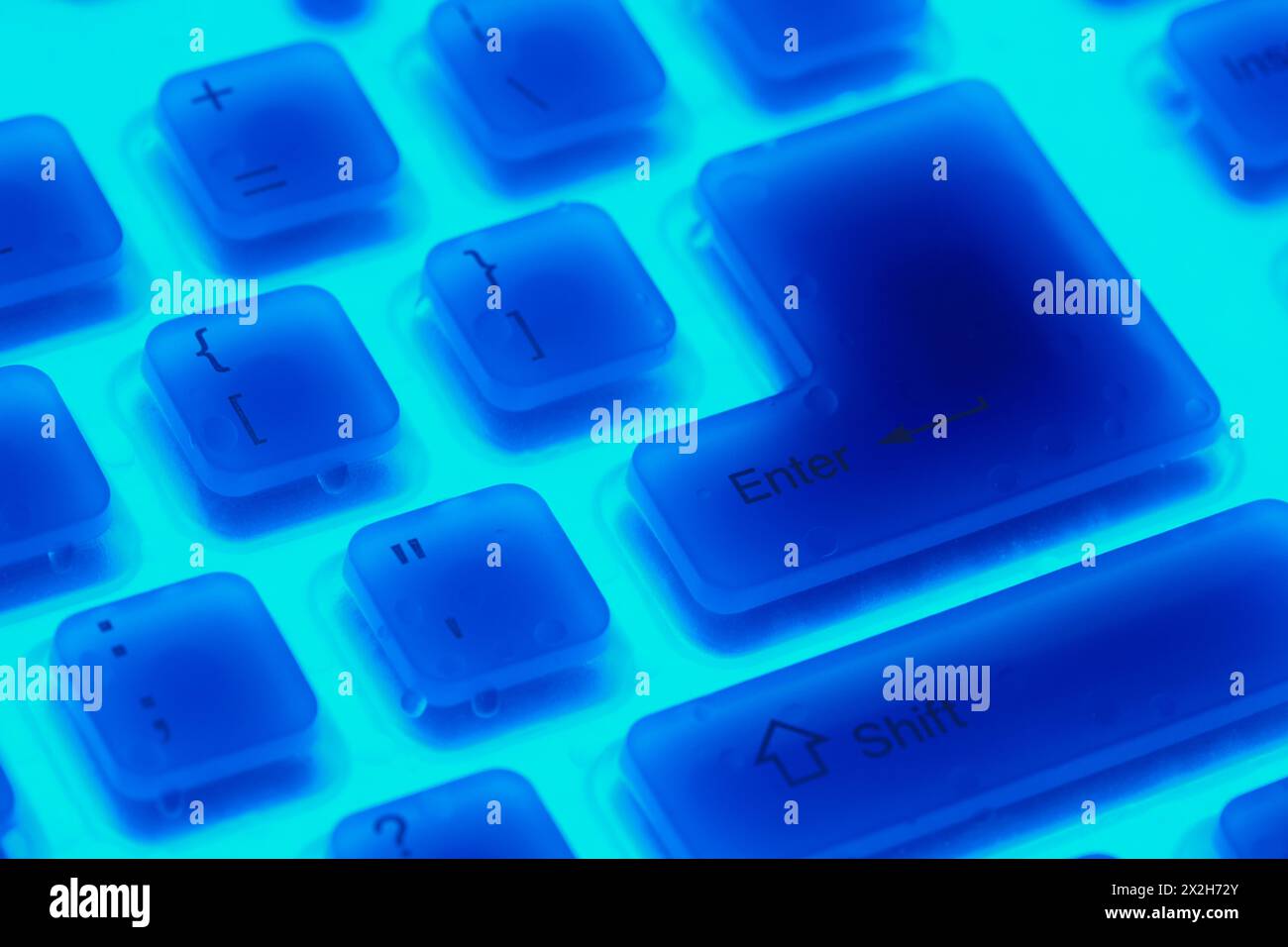 Fragment d'un clavier souple rétroéclairé bleu avec touches ENTER et SHIFT recouvertes de gouttelettes d'eau. Banque D'Images
