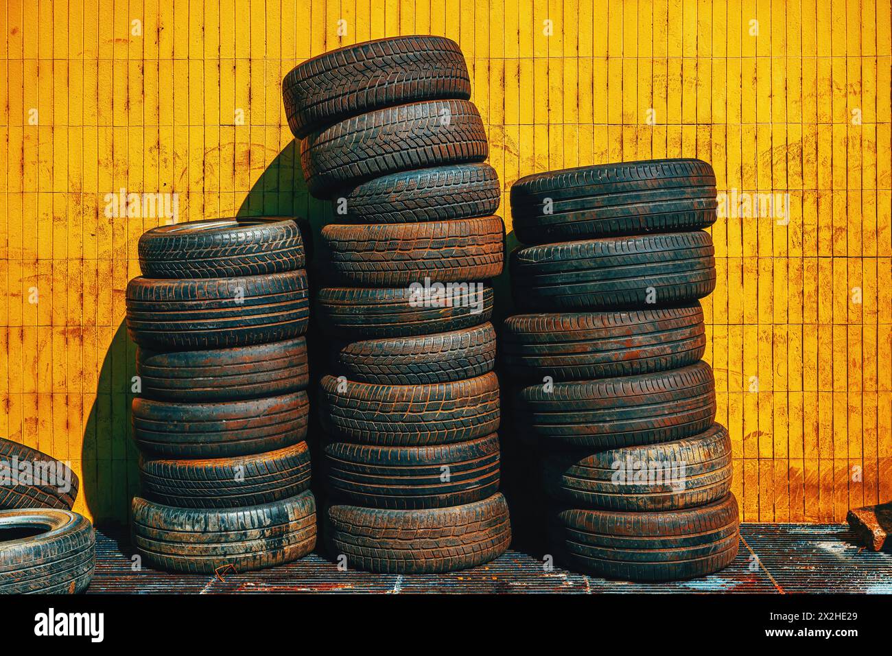 Pile de vieux pneus de voiture usagés devant l'atelier contre le mur jaune Banque D'Images
