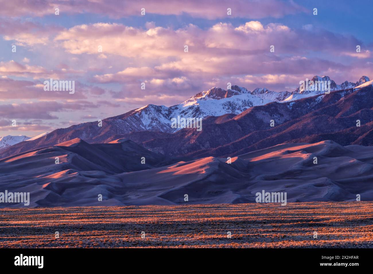 La lumière Golden Hour réchauffe les sommets des montagnes Sangre de Cristo et les sommets des dunes de sable dans le parc national Great Sand Dune, Colorado Banque D'Images