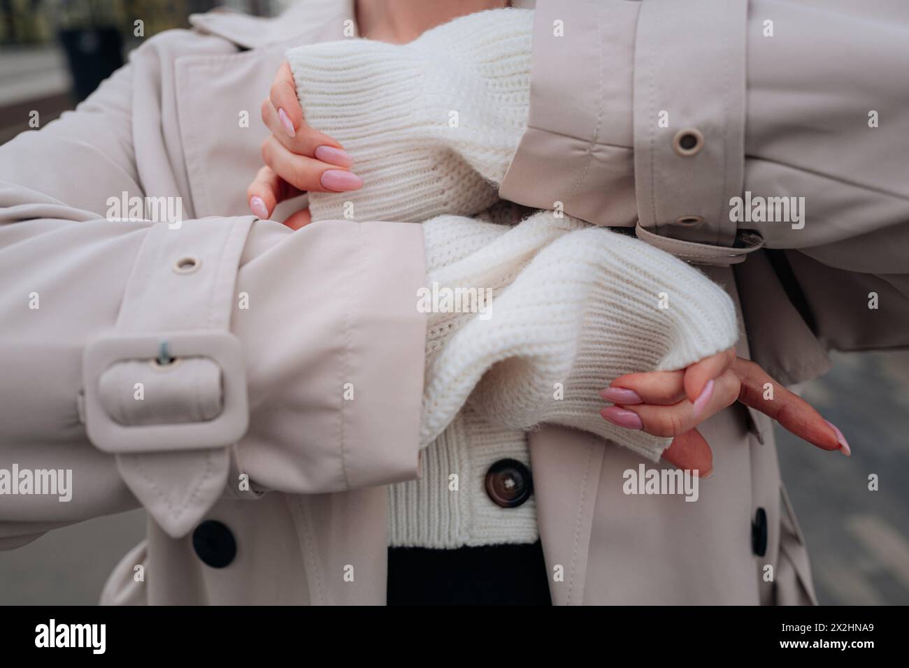 Détails de mode en tissu de style urbain d'un pull boutonné blanc tricoté et trench-coat beige pour femme. Mode urbaine contemporaine Banque D'Images