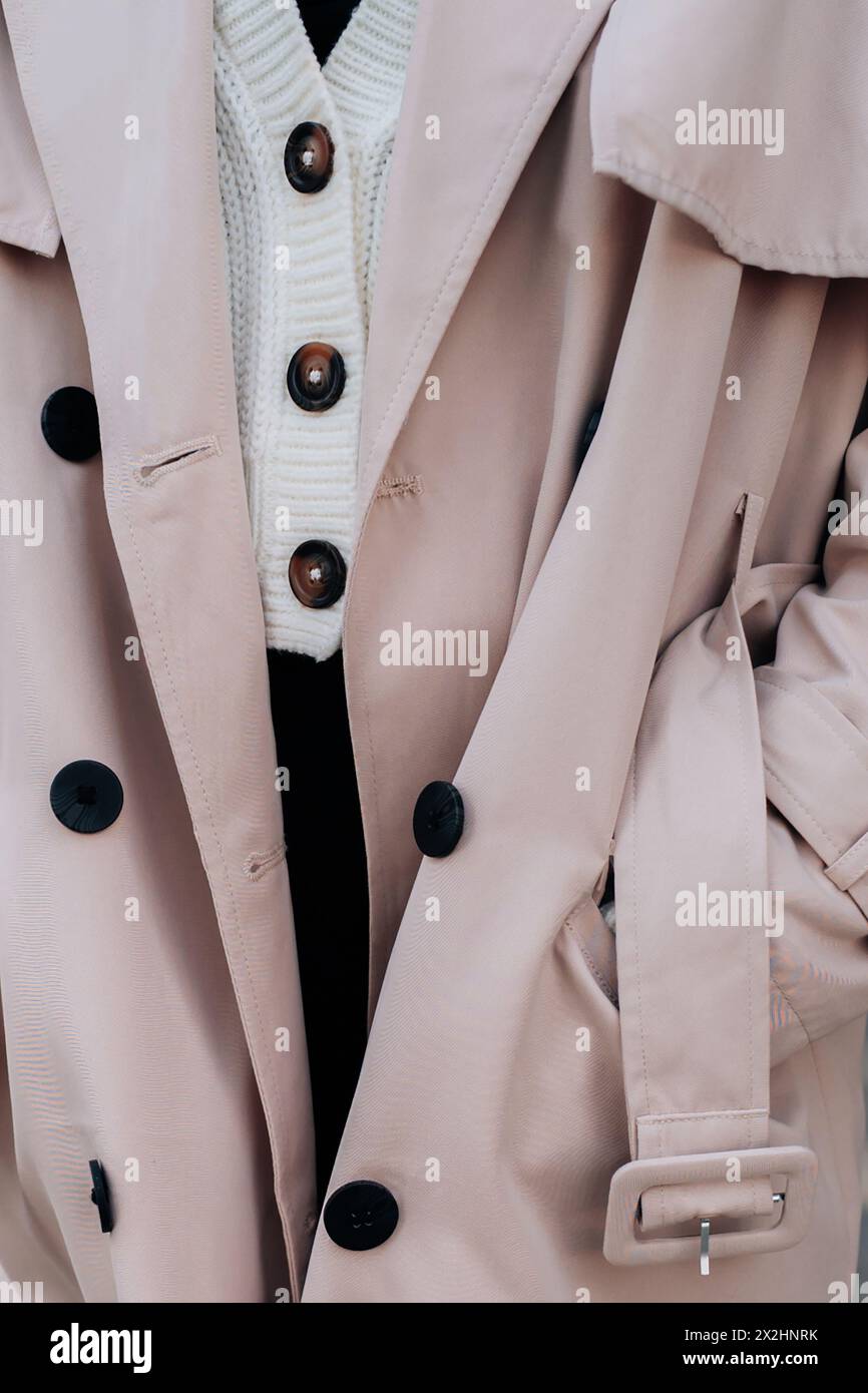 Gros plan sur les détails de mode d'un pull boutonné blanc tricoté et un trench beige pour femme. Mode urbaine contemporaine Banque D'Images