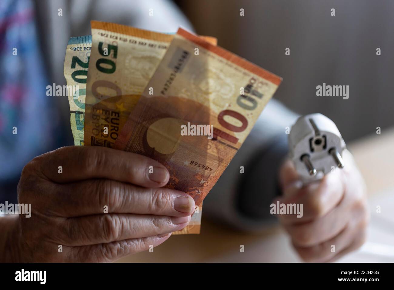 Personne âgée tenant de l'argent et un câble d'alimentation avec prise dans sa main à la maison, symbolisant les coûts de l'énergie et la pauvreté, Cologne, Rhénanie du Nord-Westphalie Banque D'Images