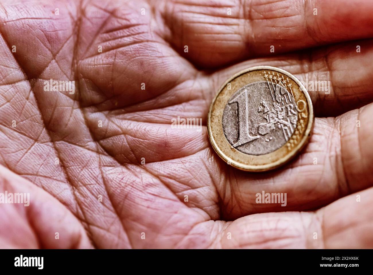 Une pièce en euros dans la main ridée d'un vieillard, symbolisant la pauvreté et la pauvreté chez les personnes âgées Banque D'Images