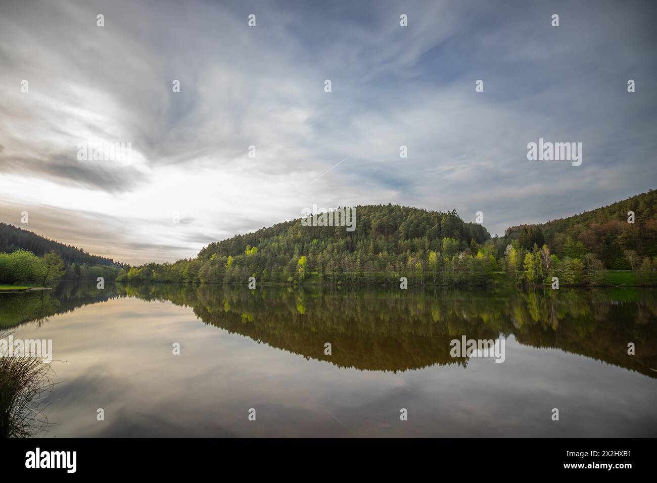 Un lac dans un paysage photographié. Un coucher de soleil et l'environnement naturel se reflètent dans l'eau du réservoir. Réservoir Marbach, Odenwald, Hesse Banque D'Images