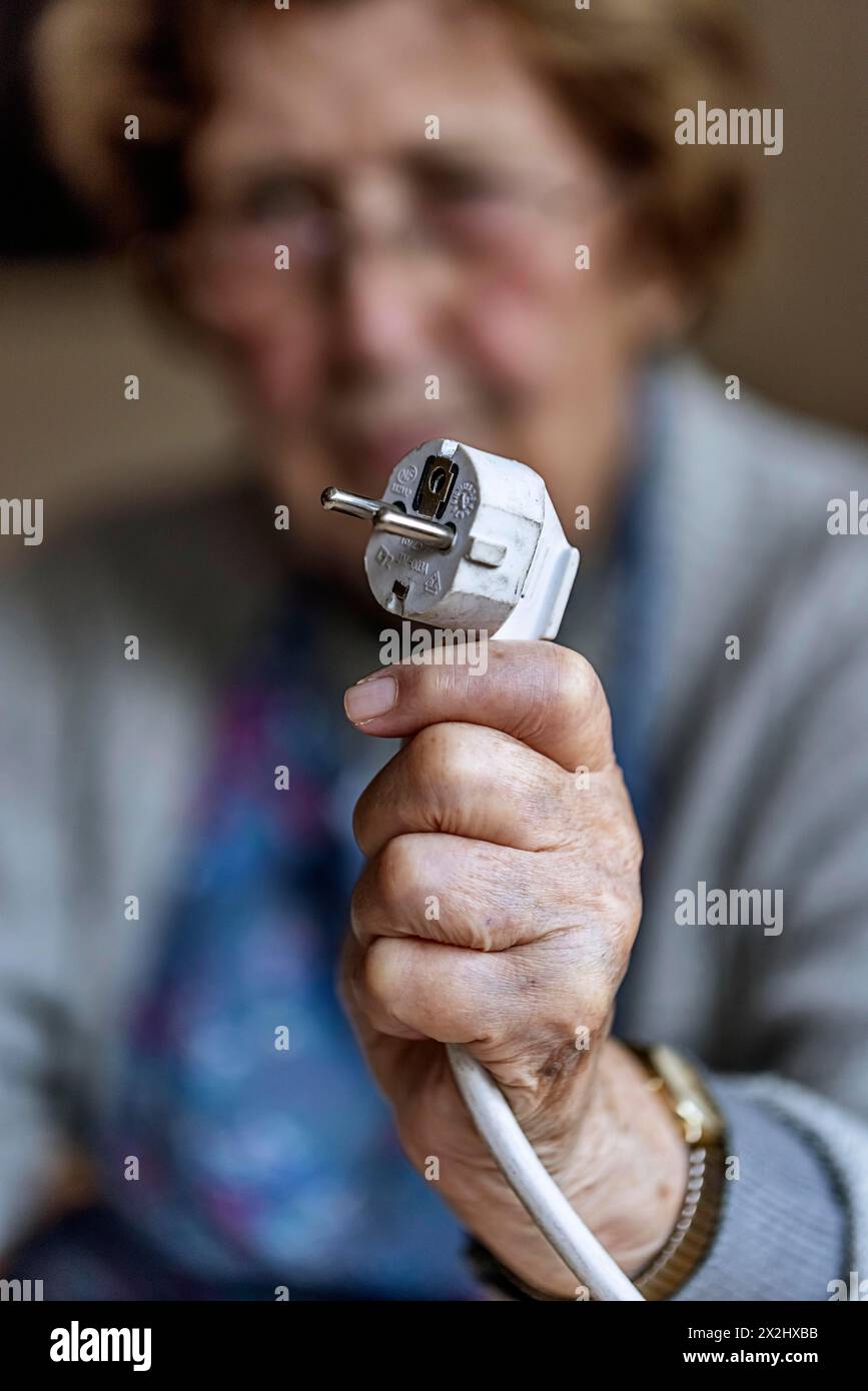 Personne âgée tenant un câble d'alimentation avec prise dans la main à la maison, symbolisant les coûts de l'énergie et la pauvreté, Cologne, Rhénanie du Nord-Westphalie, Allemagne Banque D'Images
