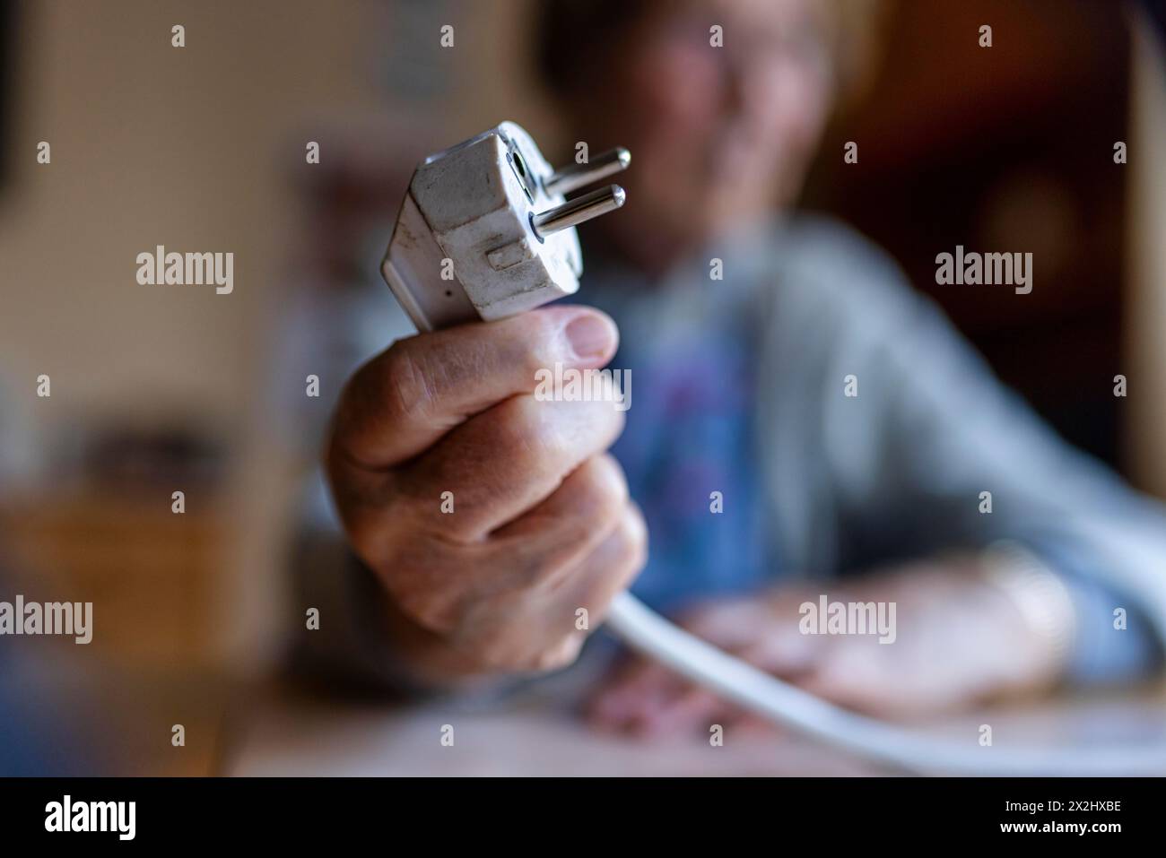 Personne âgée tenant un câble d'alimentation avec prise dans la main à la maison, symbolisant les coûts de l'énergie et la pauvreté, Cologne, Rhénanie du Nord-Westphalie, Allemagne Banque D'Images