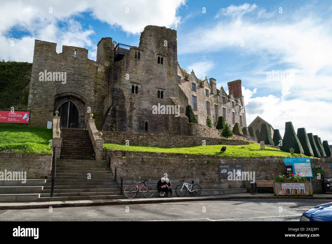 Deux cyclistes assis sous le château à Hay-on-Wye, regardant leurs téléphones Banque D'Images