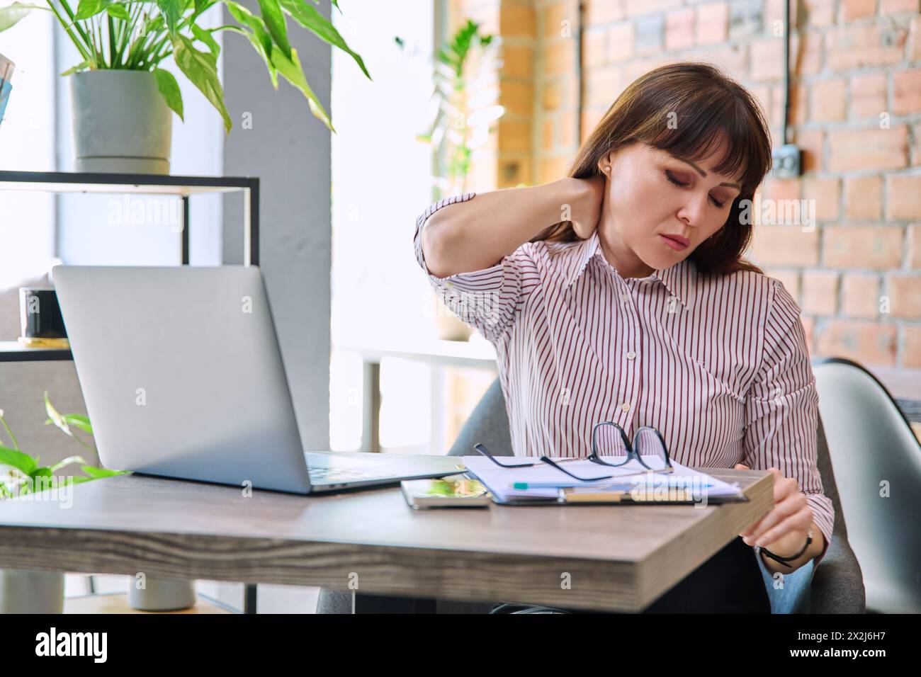 Mature fatigué inquiet femme tendue au travail éprouvant des douleurs au cou et au dos Banque D'Images