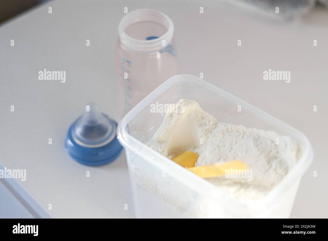 Gros plan vue de dessus du lait en poudre sec pour nourrir les bébés dans une boîte avec une pelle en plastique jaune et un biberon vide Banque D'Images