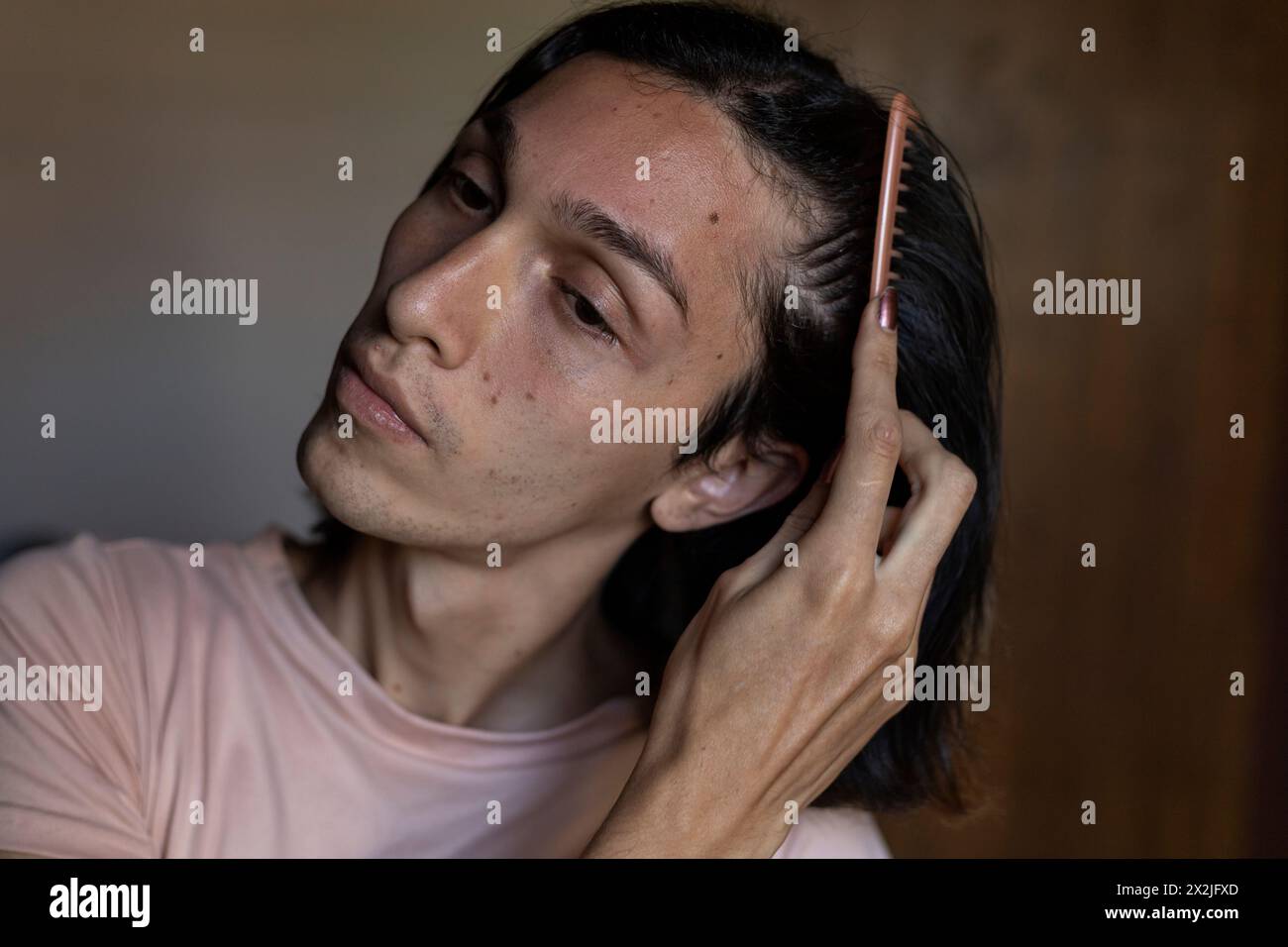 Jeune homme transgenre (22) se peignant les cheveux. Concept transgenre Banque D'Images