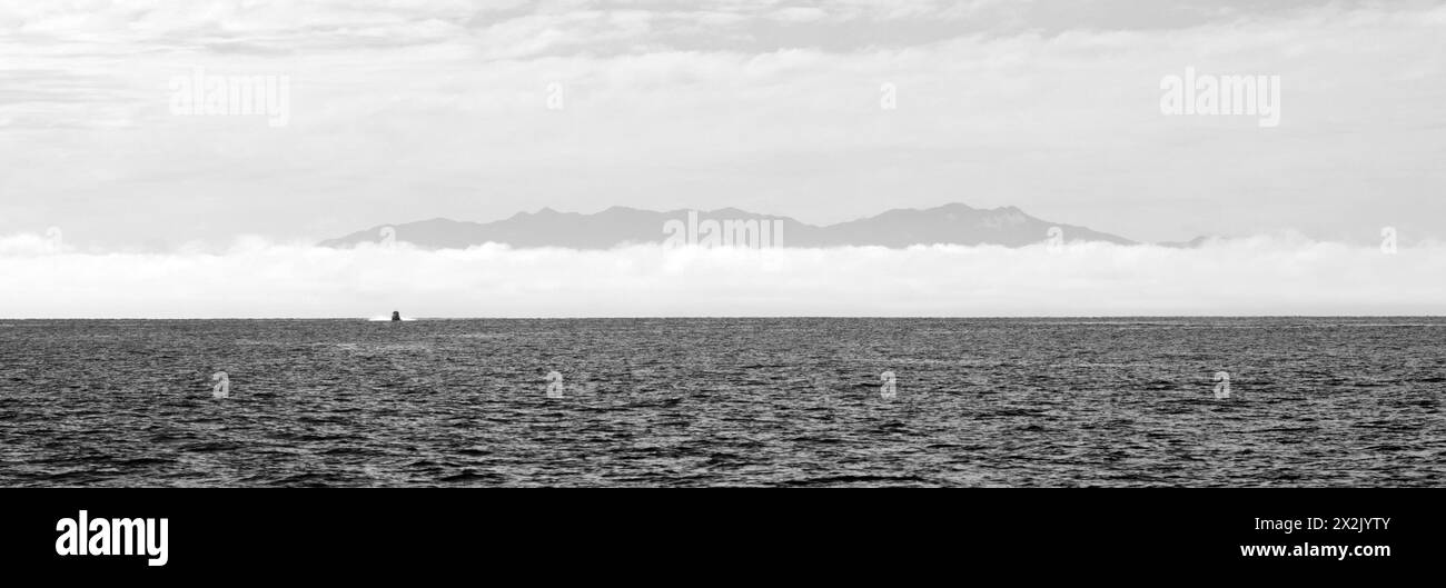 Un panorama noir et blanc de la mer, du brouillard, des chaînes et du ciel avec un lancement lointain à l'horizon. Banque D'Images