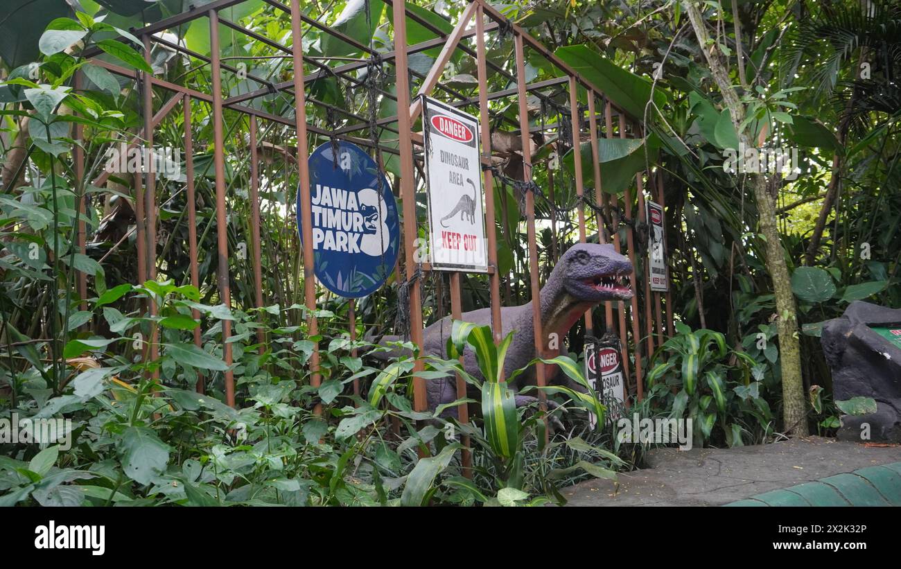 Statue de dinosaure mise en cage dans une cage avec écriture dangereuse et fond de forêt à Dino Park Jatim Park 3 Batu Banque D'Images