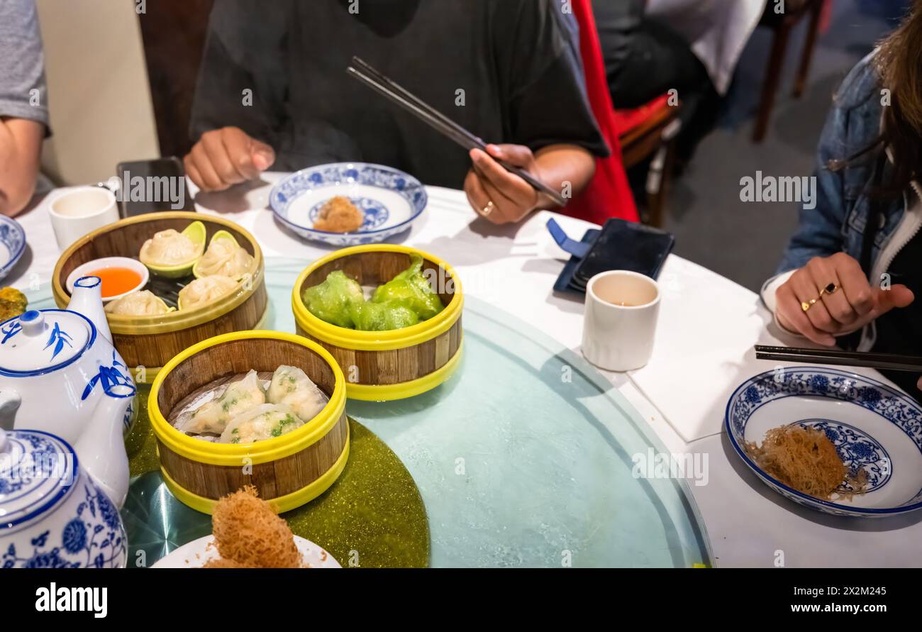 Mains tenant des baguettes. Yumcha, dim sum dans des cuiseurs à vapeur en bambou. Cuisine chinoise. Banque D'Images