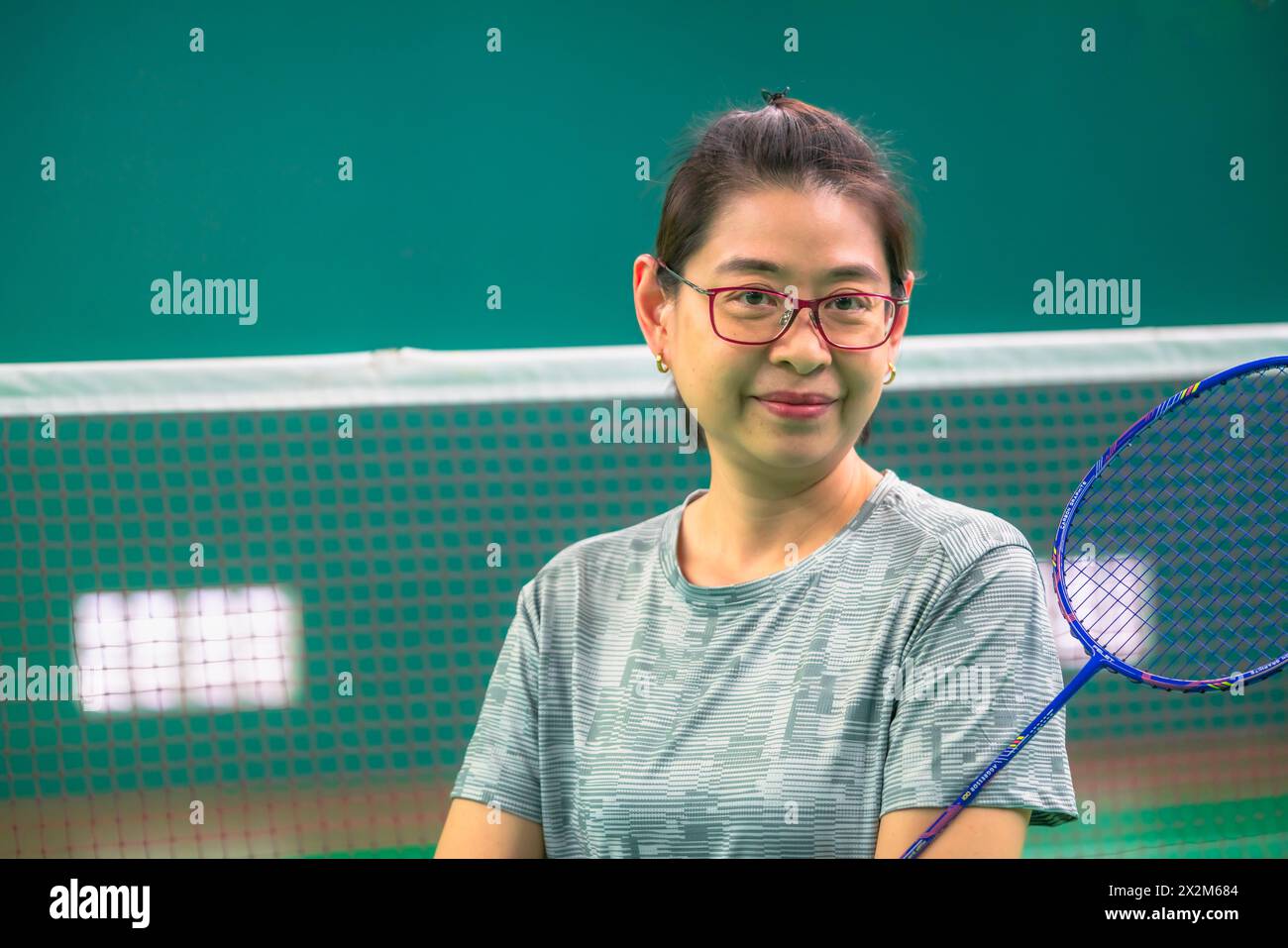 Portrait d'une femme asiatique d'âge moyen sur un court de badminton, tenant une raquette de badminton, portant des lunettes, souriant et regardant la caméra, l'espace Banque D'Images