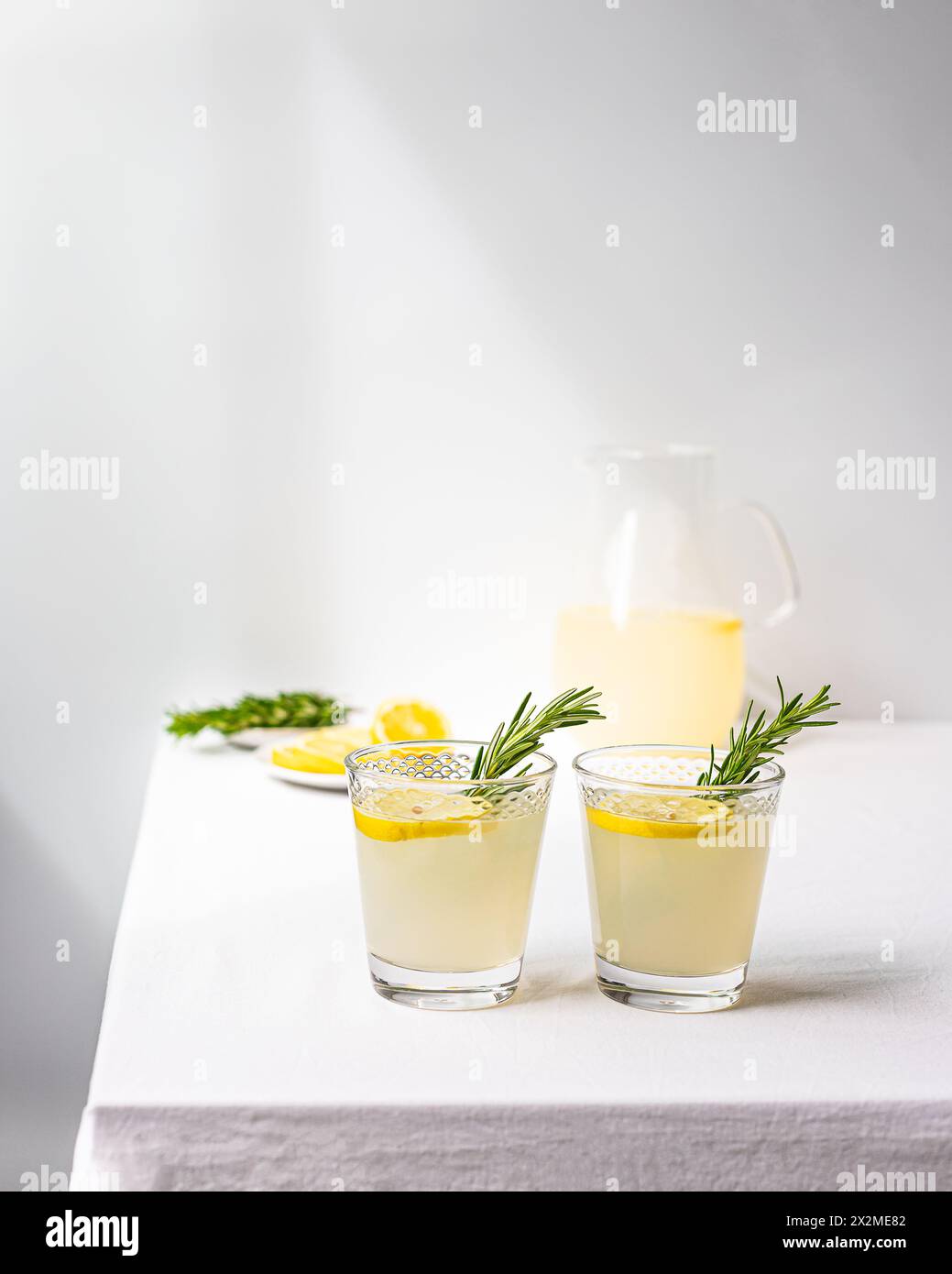 Deux verres de limonade maison avec des brins de romarin et un pichet en arrière-plan sur une table blanche, offrant un look frais et propre Banque D'Images