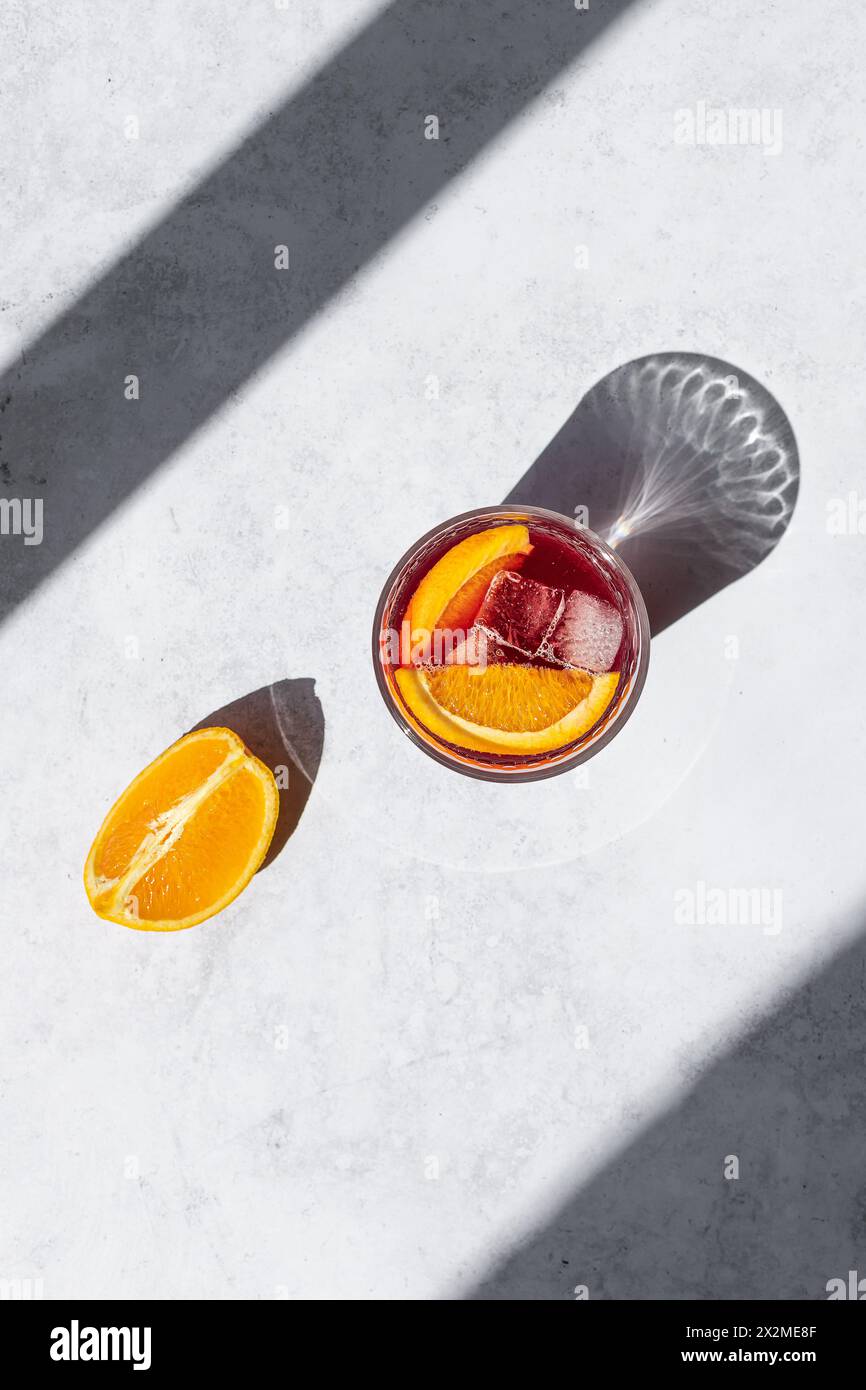 Un verre vibrant de Tinto de Verano, garni d'une tranche d'orange, baigne dans la lumière du soleil, projetant une ombre réfléchissante sur une surface texturée Banque D'Images