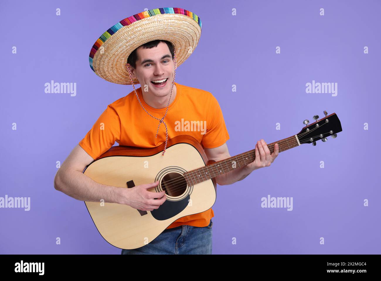 Jeune homme au chapeau sombrero mexicain jouant de la guitare sur fond violet Banque D'Images