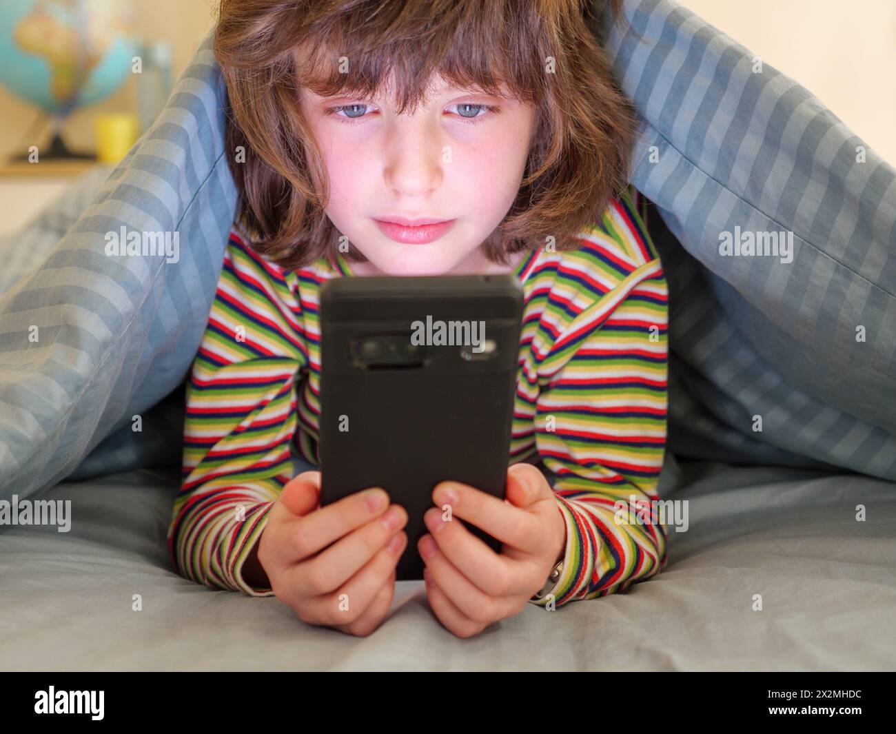 Jeune fille regardant l'écran de son téléphone portable dans sa chambre Banque D'Images