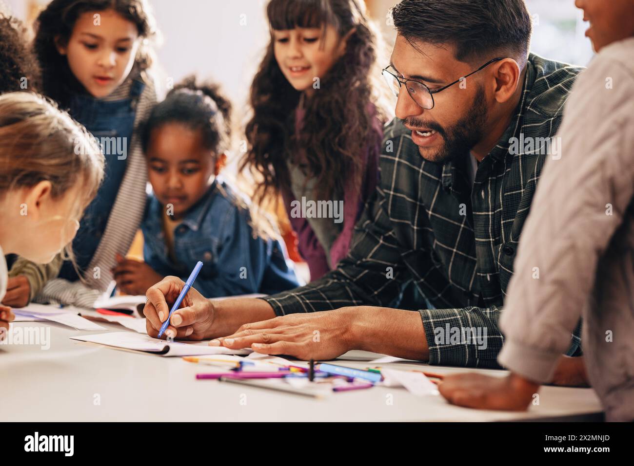 L'homme enseigne à ses élèves comment dessiner dans une classe d'école primaire. Cet éducateur d'école primaire montre à ses enfants comment utiliser un crayon à colorer. Enseignement Banque D'Images