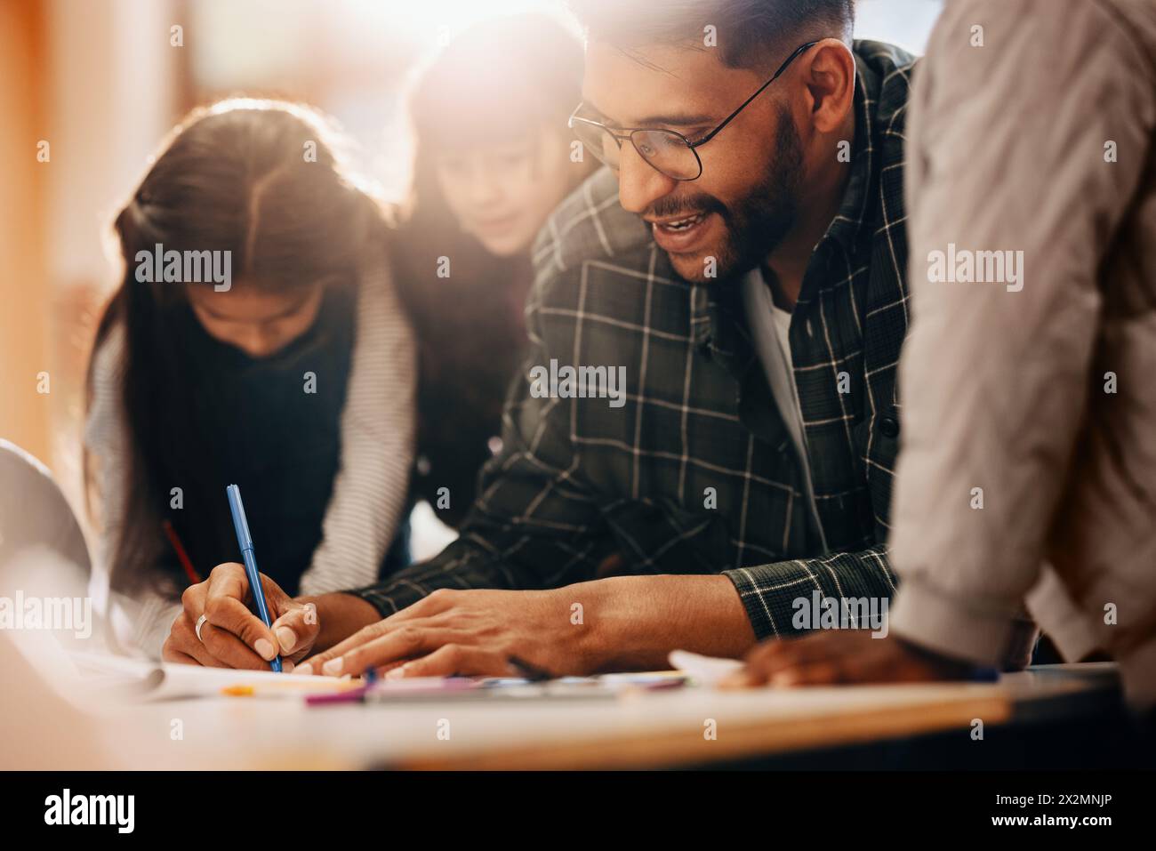 Cours de dessin à l'école primaire. Le professeur montre à ses élèves comment utiliser un stylo à colorer. L'homme encadre un groupe d'enfants dans un développement précoce de l'enfant Banque D'Images