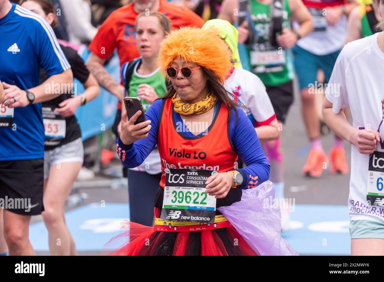 Viola Lo de Hong Kong participant au TCS London Marathon 2024 en passant par Tower Hill, Londres, Royaume-Uni. Personne avec un canal de médias sociaux au téléphone Banque D'Images