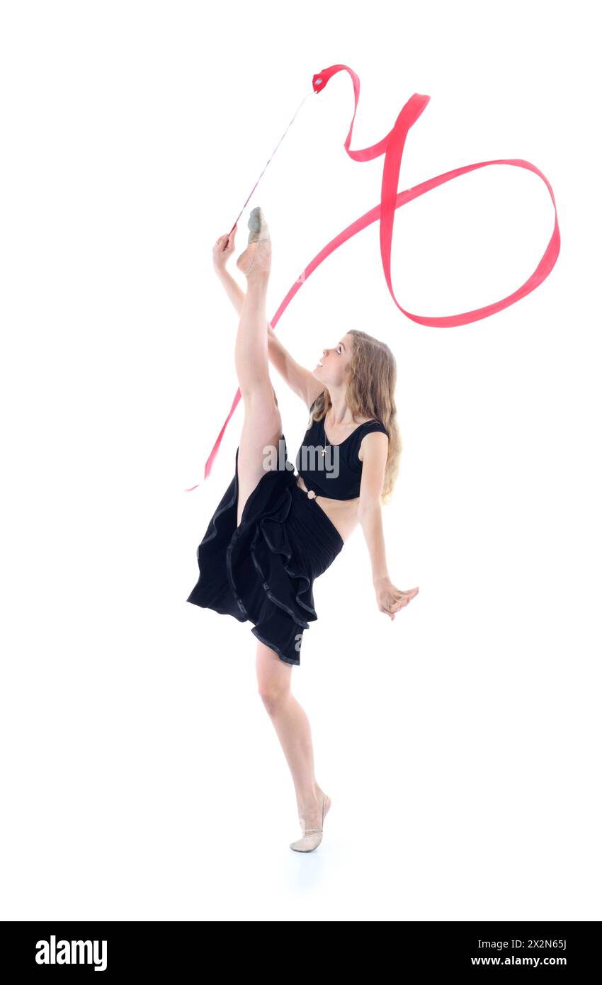 Gymnaste gracieux en robe noire avec ruban rouge se tient sur une jambe et l'autre jambe soulevée haut isolé sur fond blanc. Banque D'Images