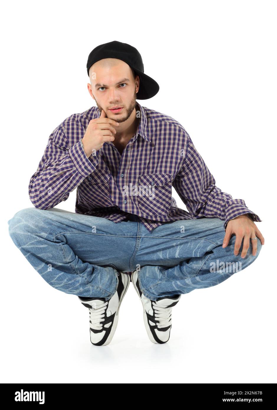 Jeune rappeur en Jean et chemise à carreaux squatting isolé sur fond blanc. Banque D'Images