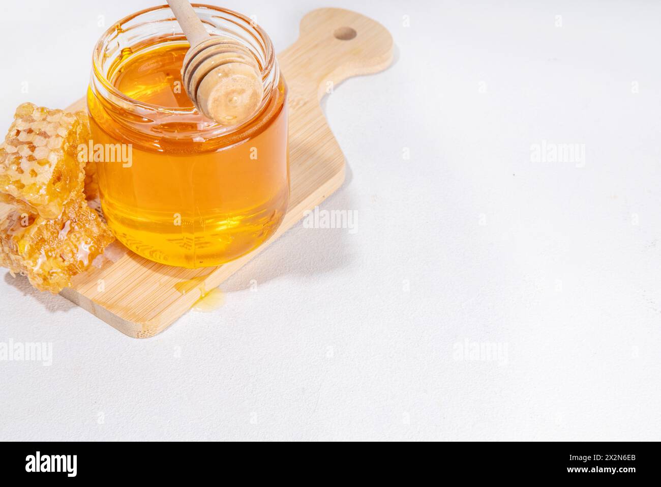 Miel de fleur dorée dans un petit pot, avec cuillère à miel et nid d'abeilles Banque D'Images